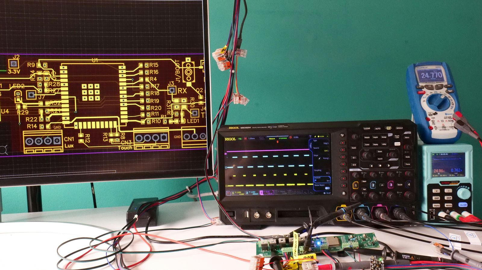 Werkbank met printontwerp op het scherm, oscilloscoop en multimeter